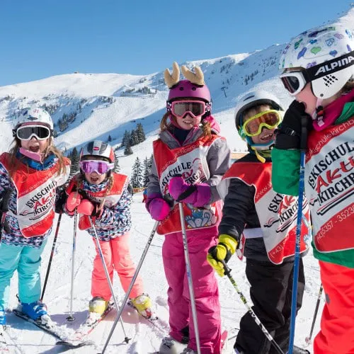 Children in a ski lesson group wearing helmets and goggles on the slope