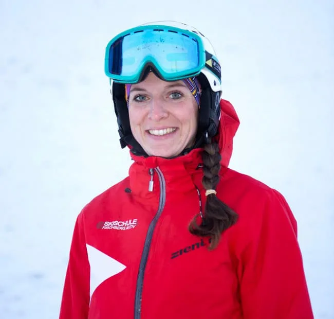 Woman smiling in ski gear with goggles against snowy backdrop