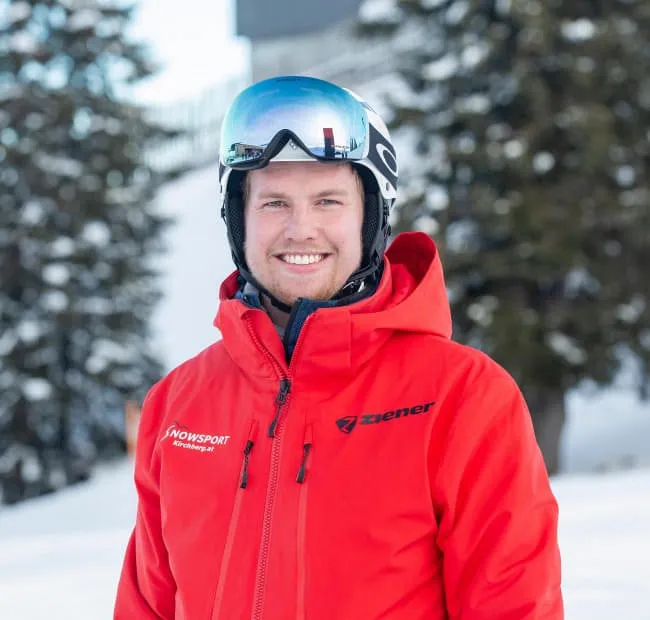 Smiling ski guide in red jacket, snow in the background