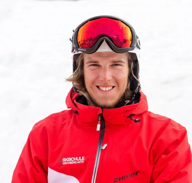 Smiling skier in red jacket with goggles in the snow.