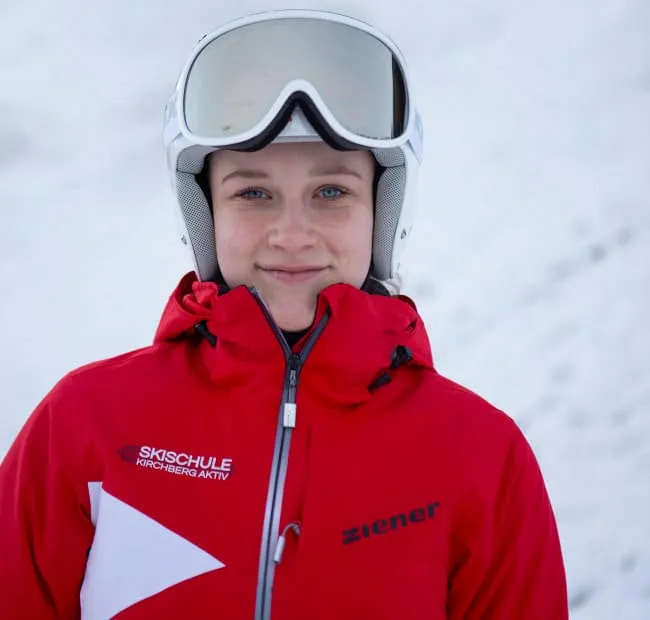 Smiling person in red ski jacket with ski helmet