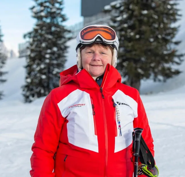 Woman in red ski jacket holding skis in the snow
