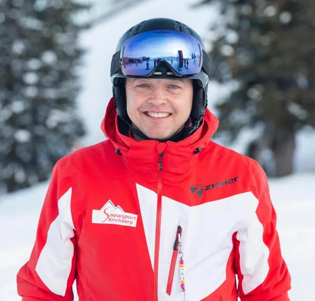 Smiling skier in a red jacket at a snowy location