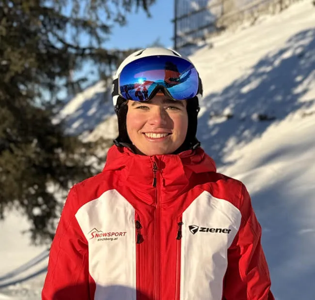 Skier in red jacket with goggles in snowy landscape.