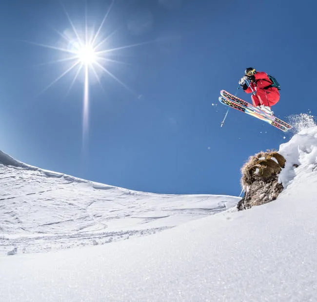 Skier jumping over snow with a bright sun in the sky