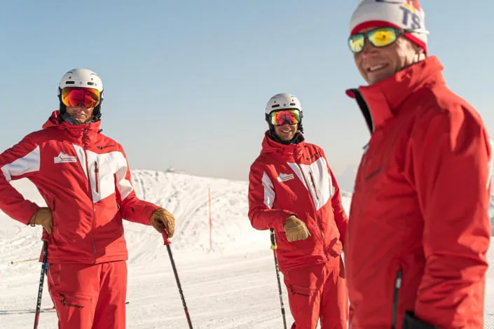 Drei Skilehrer in roten Anzügen auf der Piste